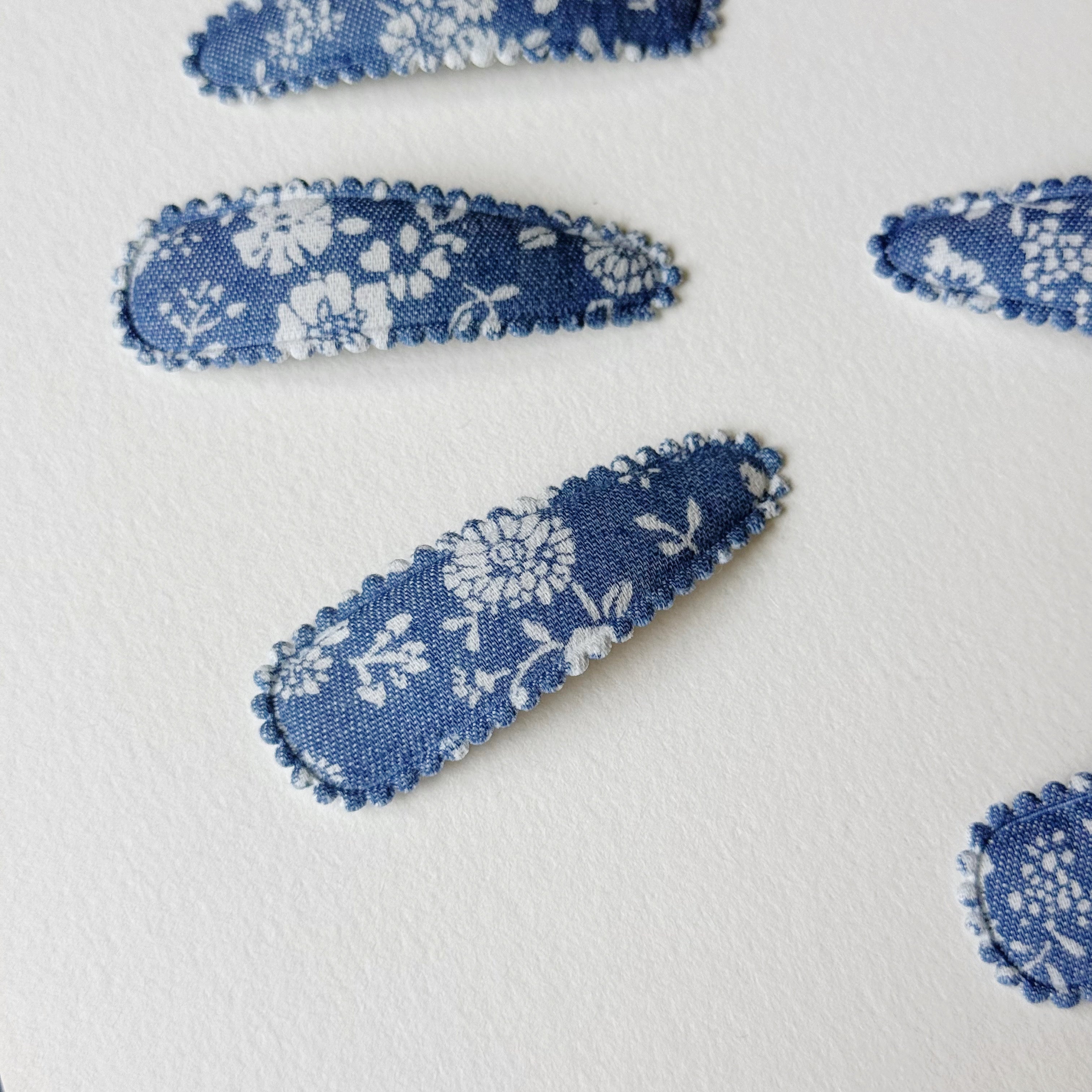 Blue and white floral fabric hair clips arranged on a textured white background.