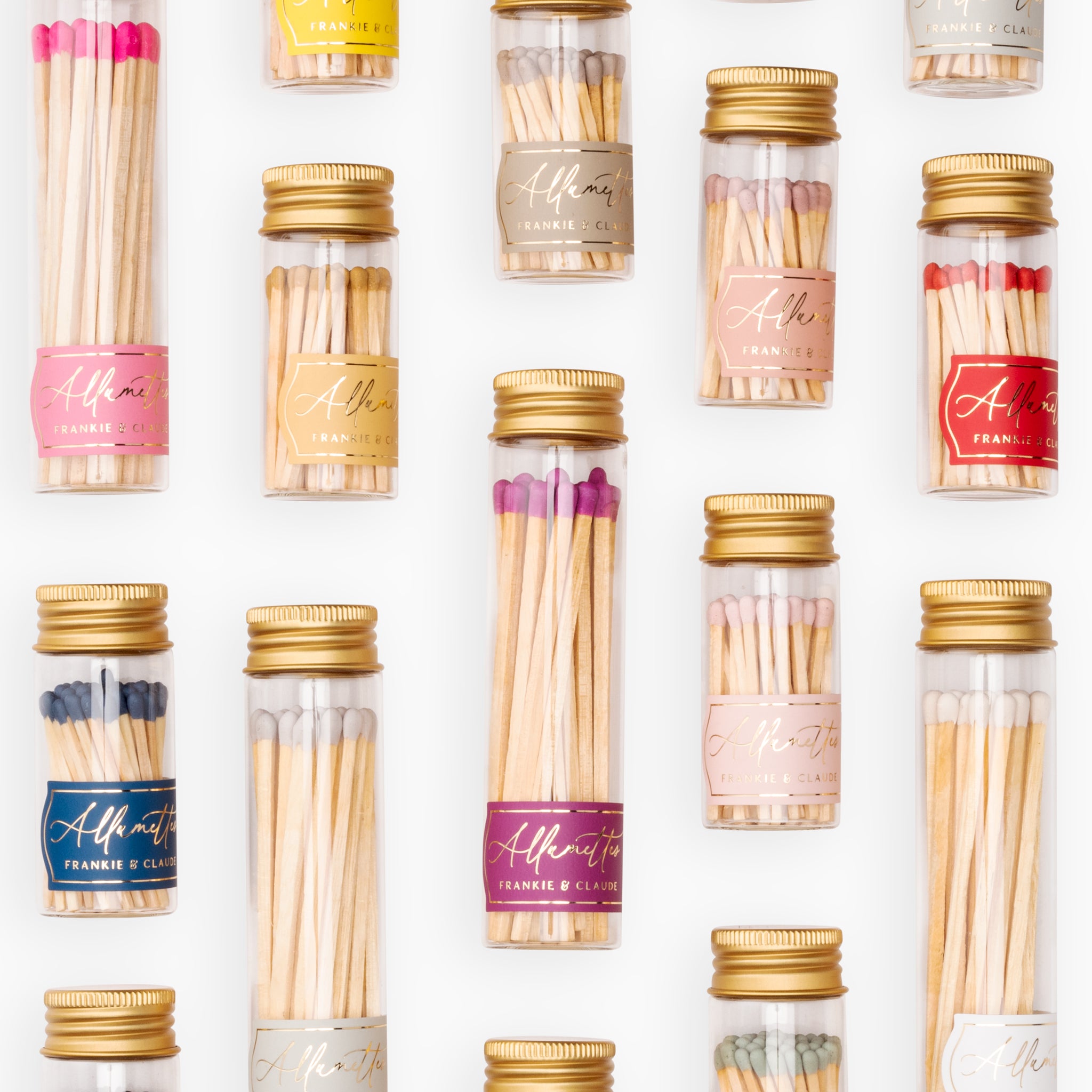 Collection of Frankie & Claude Allumette Match Jars in a variety of colors including navy, honey gold, blush pink, and more, elegantly displayed in clear glass jars with geometric gold foil labels and metallic lids.