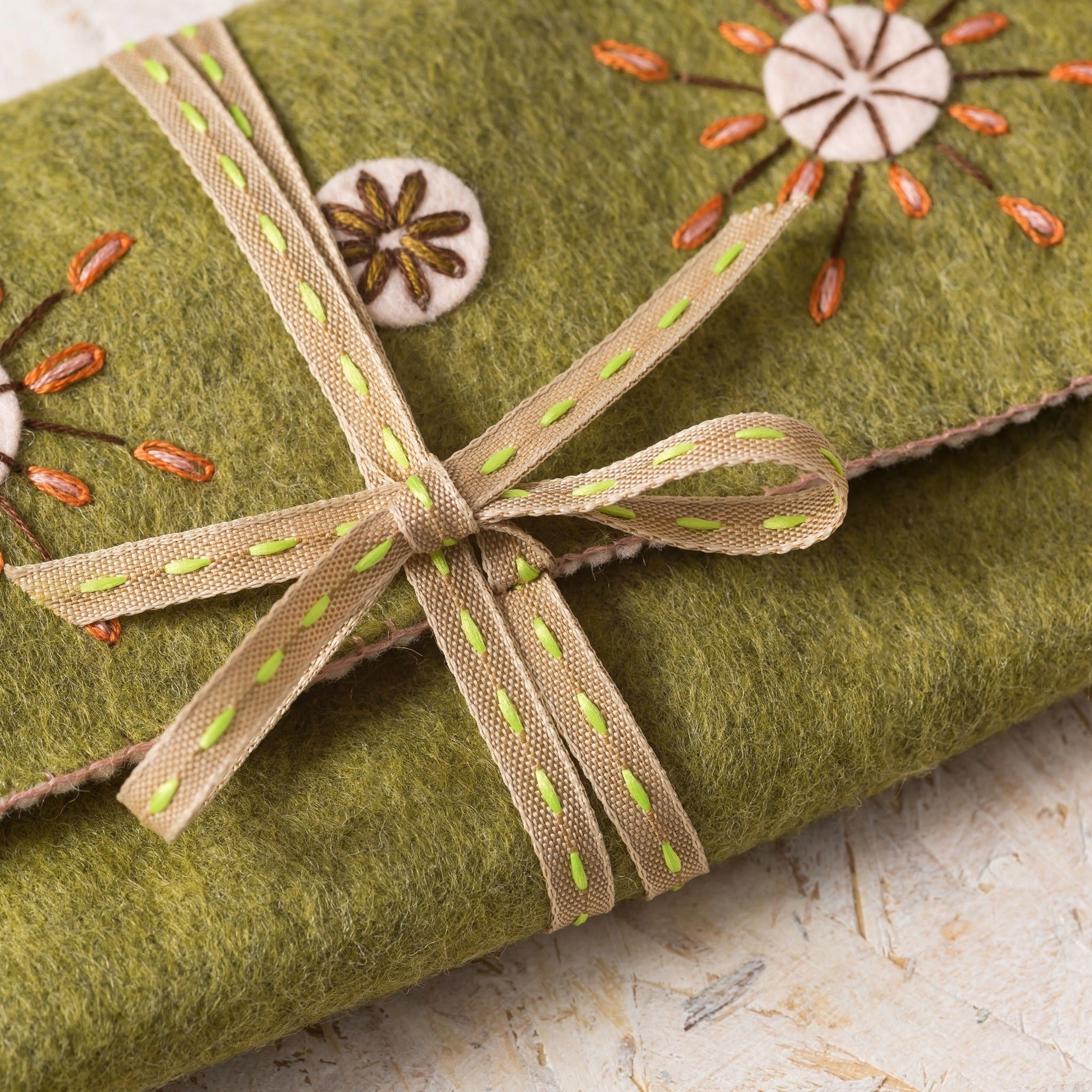 Artisanal moss-green felt Sewing Roll with a dotted beige ribbon featuring subtle green accents, complemented by hand-embroidered floral buttons and delicate burnt-orange stitch details, presented on a rustic wooden backdrop.