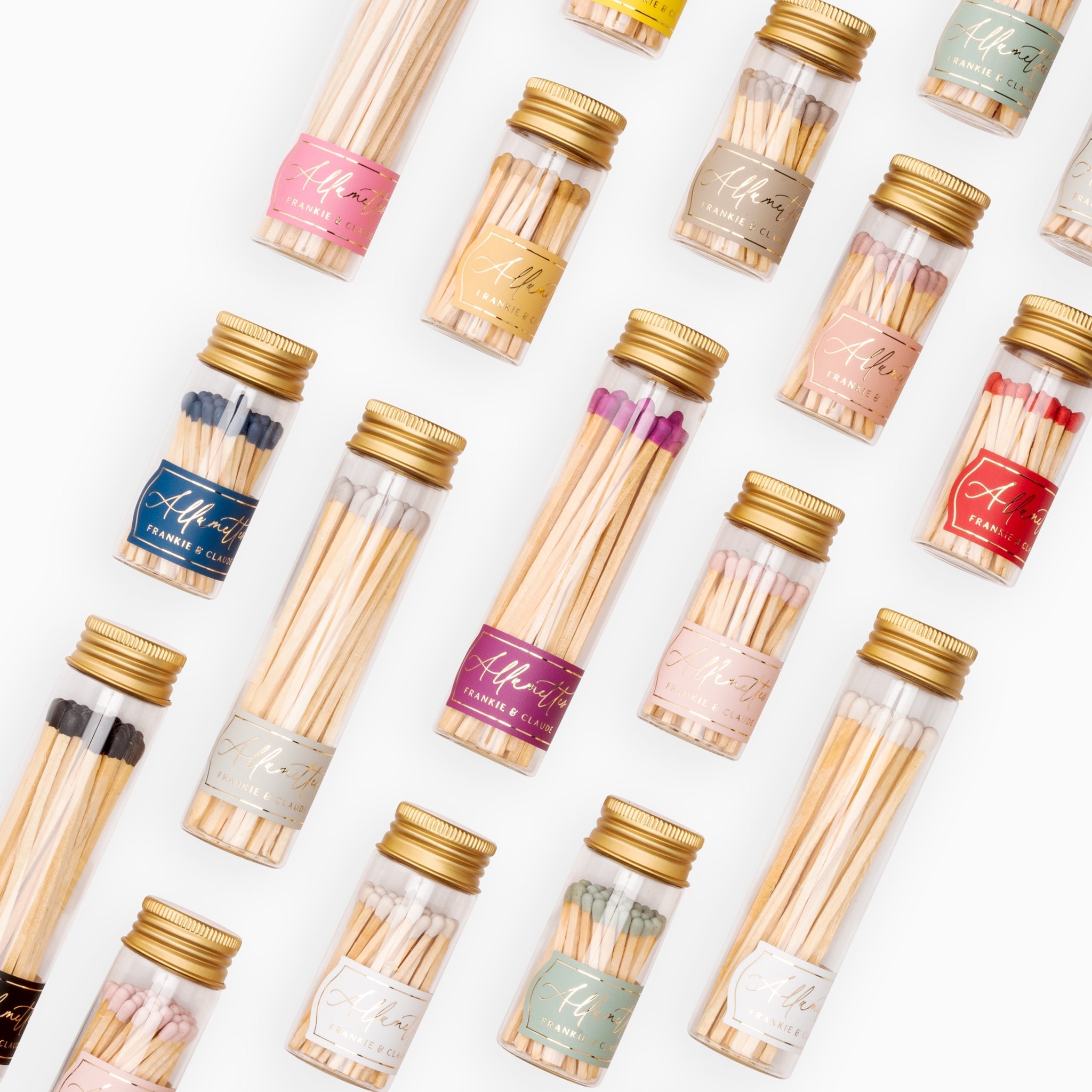 A variety of Frankie & Claude Allumette Match Jars laid out in a grid, featuring match tip colors like navy, blush pink, red, classic white, violet purple, sage green, dusty rose, driftwood, bright yellow, and honey gold in clear glass jars with golden screw-on lids.