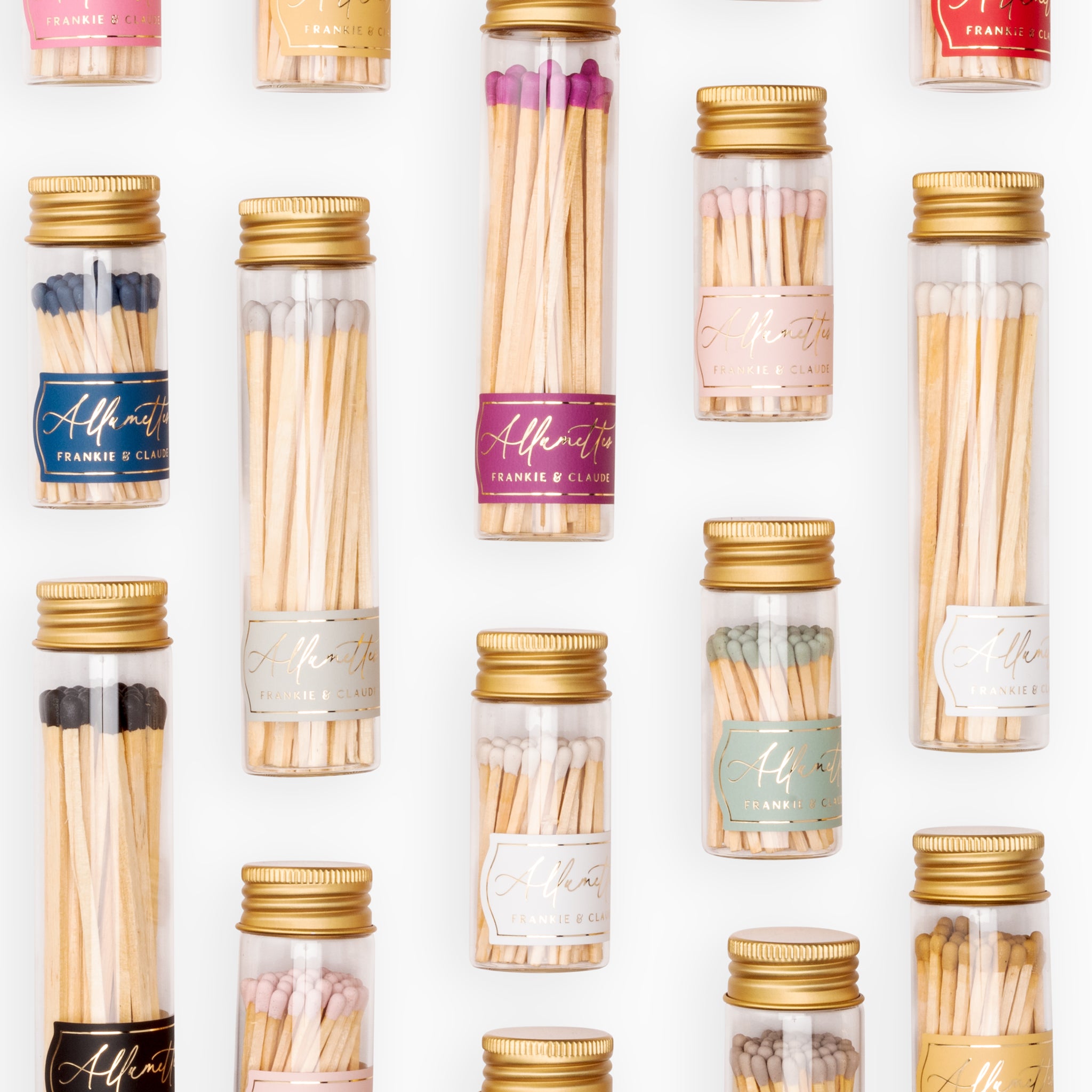 Collection of Frankie & Claude Allumette Match Jars in a variety of colors including navy, honey gold, blush pink, and more, elegantly displayed in clear glass jars with geometric gold foil labels and metallic lids.