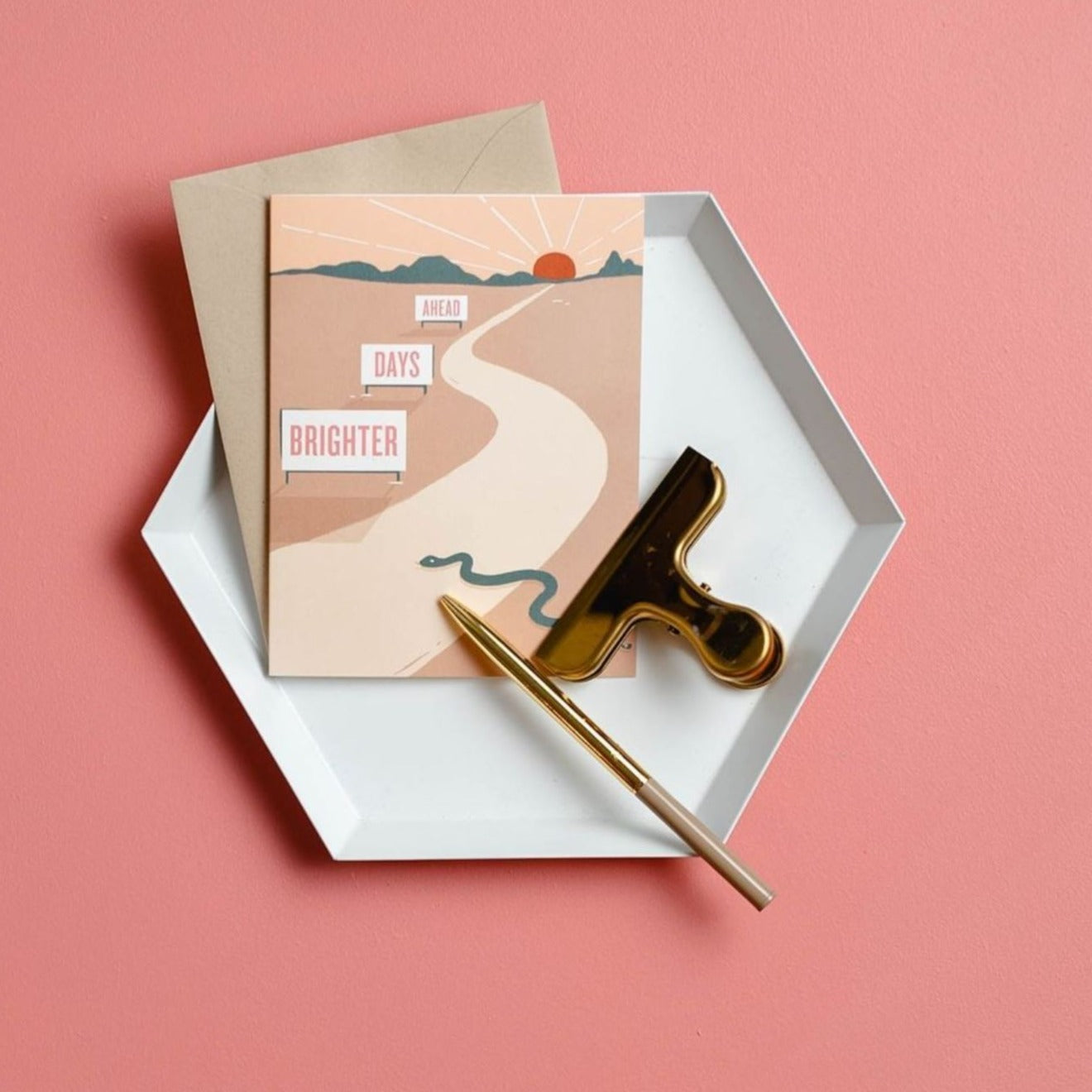 Illustrated encouragement card on premium warm white cardstock, featuring a desert scene with a snake and a setting sun, accompanied by the words 'Brighter Days Ahead. The card is sitting in a white tray on a pink piece of paper in the background.