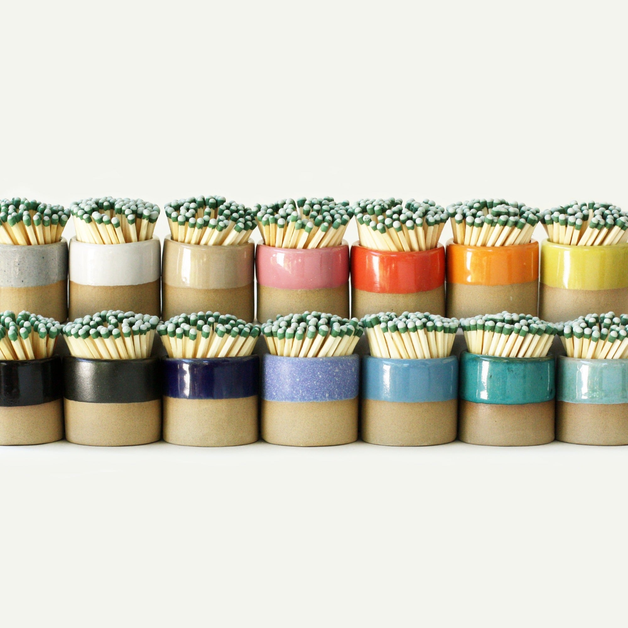 Collection of colorful ceramic match strikers, including a rainbow of colors of the ceramic match striker, all holding long matches.