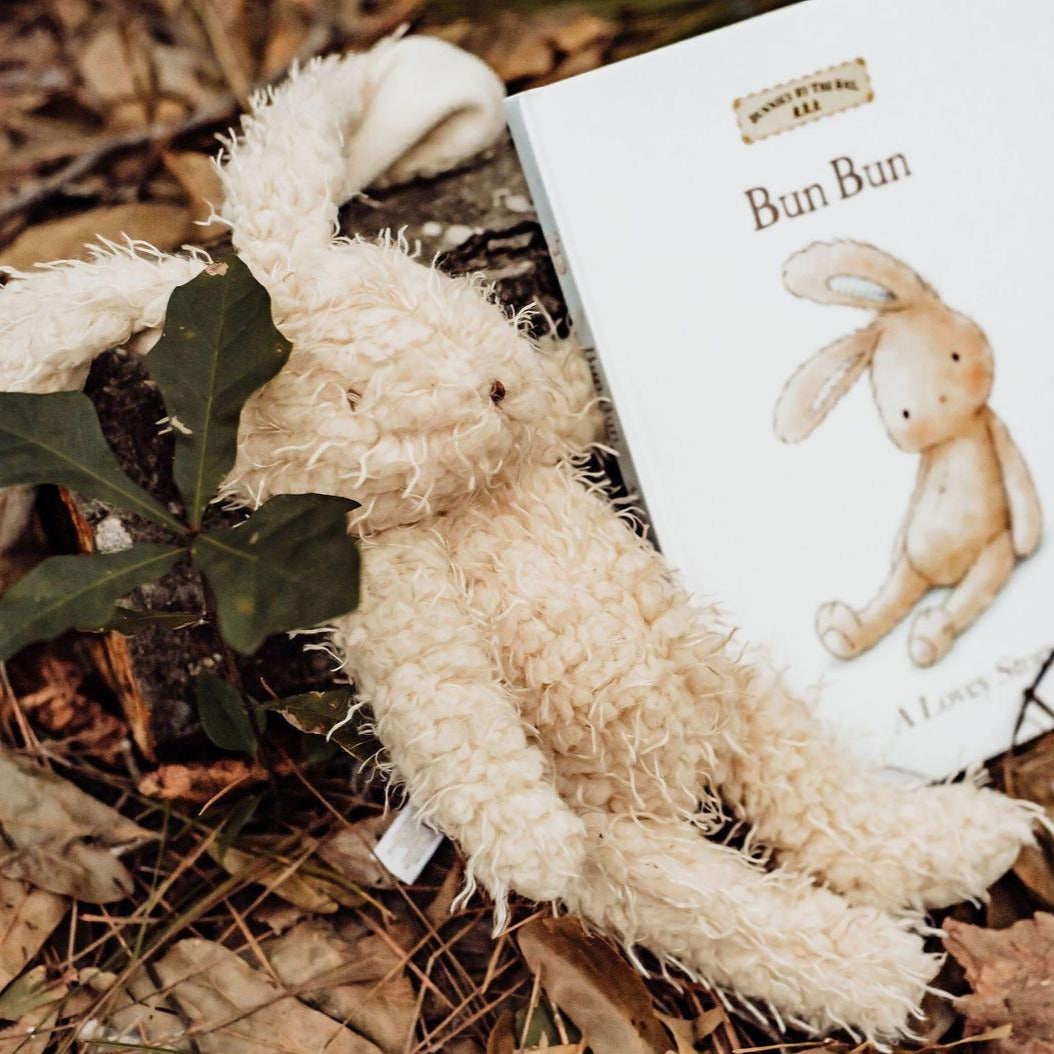 Harey the Plush Rabbit nestled next to a storybook, showcasing its warm almond scraggly fur and handcrafted embroidered face.