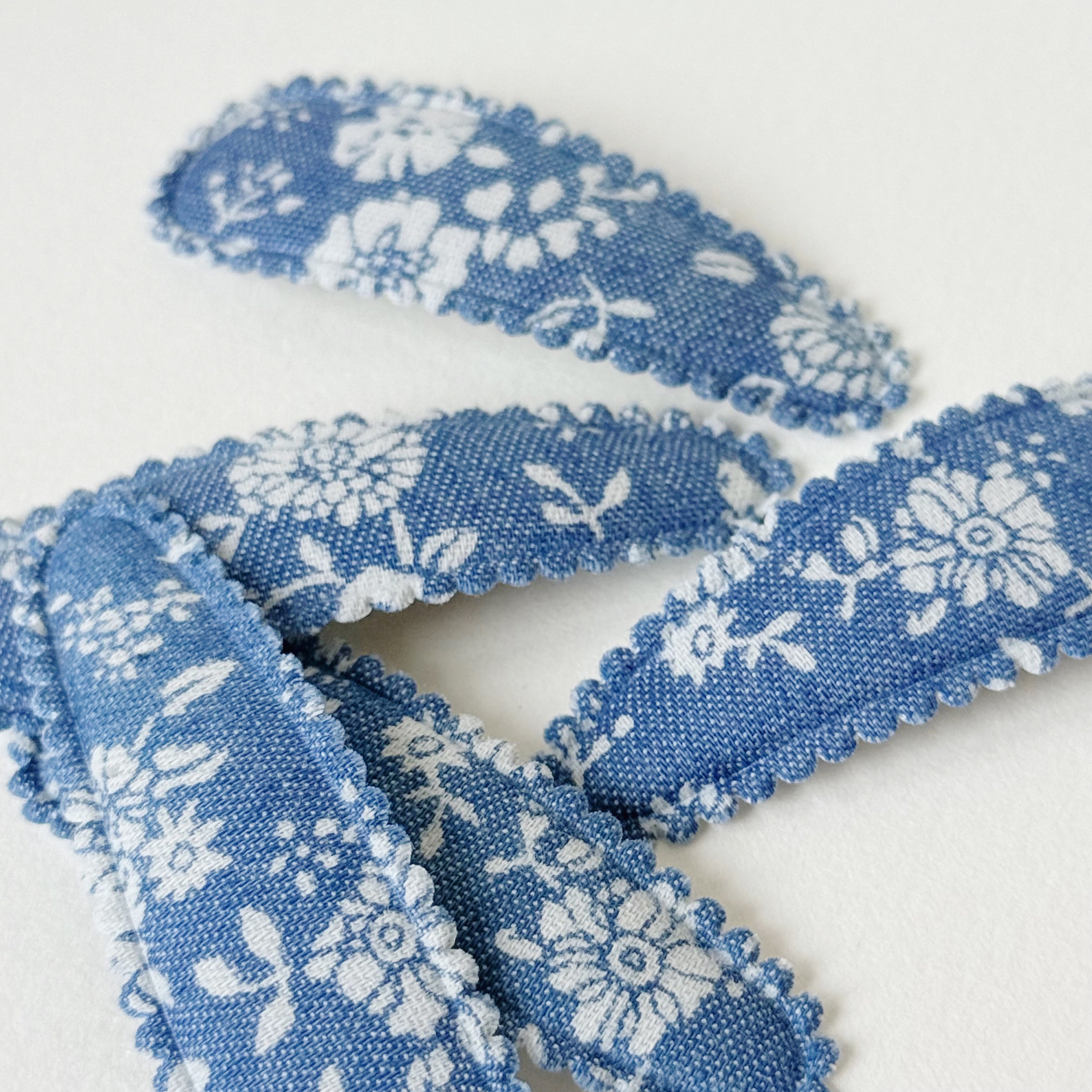 Three fabric hair claw clips with a blue and white floral pattern and frayed edges, arranged on a plain white background.