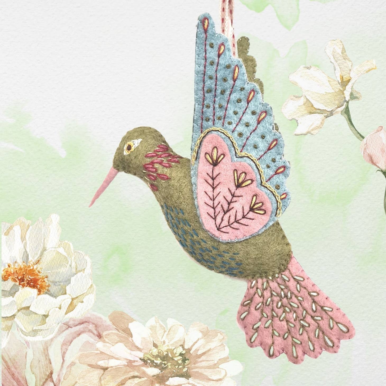 "Hand-painted watercolor illustration of the 'Hummingbird Felt Craft Mini Kit' by Corinne Lapierre, showcasing a detailed hummingbird with vibrant blue wings and pink heart-shaped patterns, nestled among delicate white blossoms.