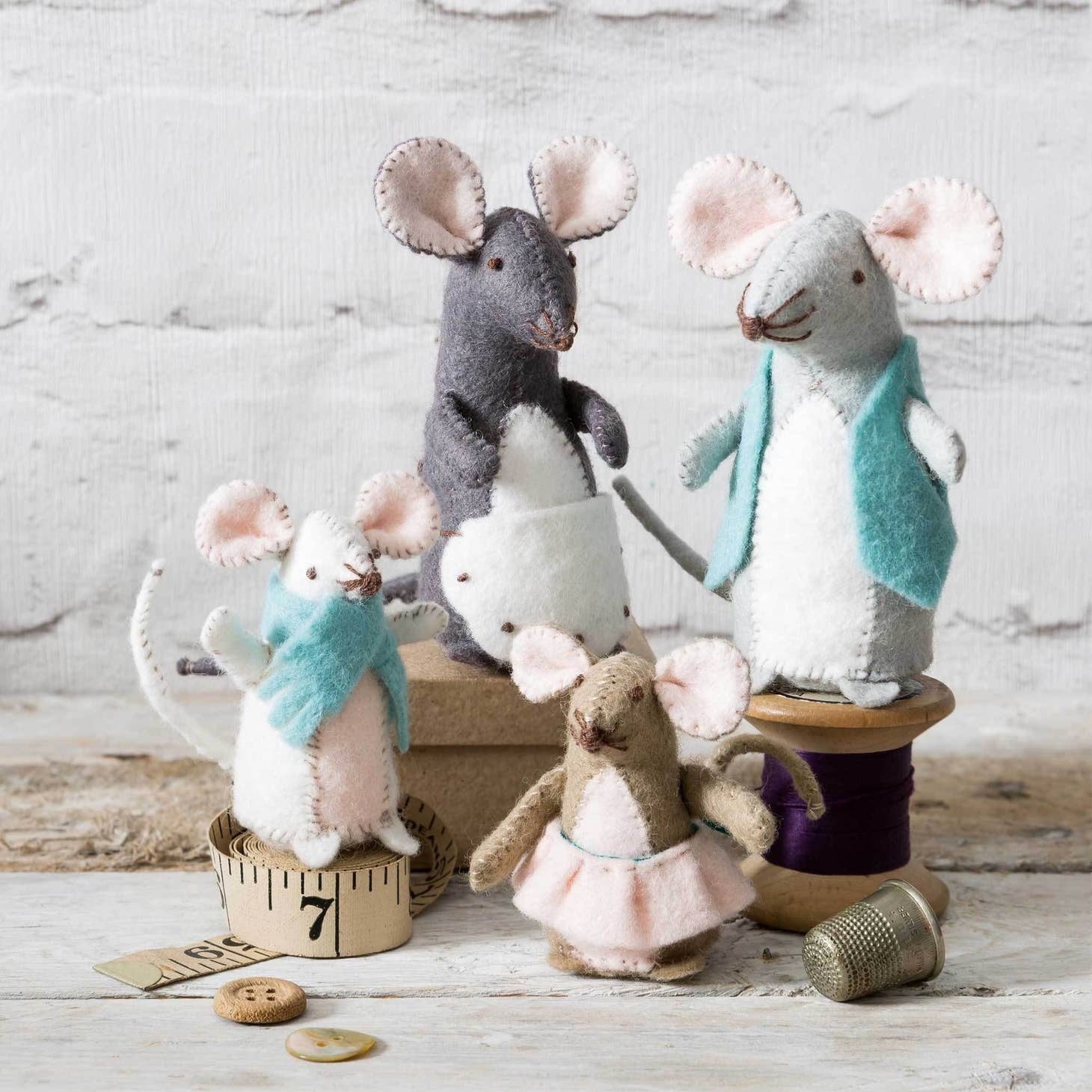 Handcrafted felt mouse family with two adult mice and two baby mice, each adorned with unique clothing items, posed against a rustic white wooden background with sewing accessories.