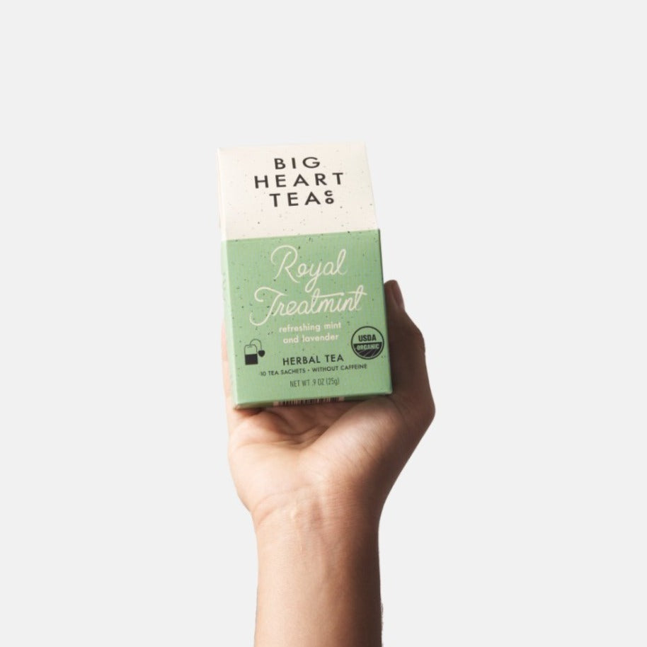Hand holding a mint green box of Royal Treatmint tea, the perfect solution for caffeine junkies. This adrenal-balancing blend features organic spearmint, peppermint, lavender, tulsi, and gingko leaf. Not only does it restore mind and body balance, but it also combats coffee breath. A soothing and invigorating mix for the over-caffeinated.
