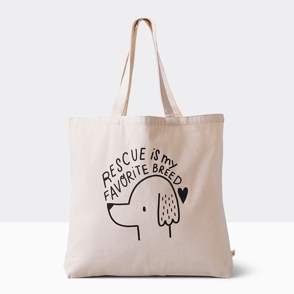 Spacious cotton canvas tote bag featuring a heartwarming dog illustration and the message 'Rescue is my favorite breed,' perfect for eco-conscious pet lovers. Bag is 17.5" wide and 15.5" tall with 10" drop handles, sitting on a plain white surface.