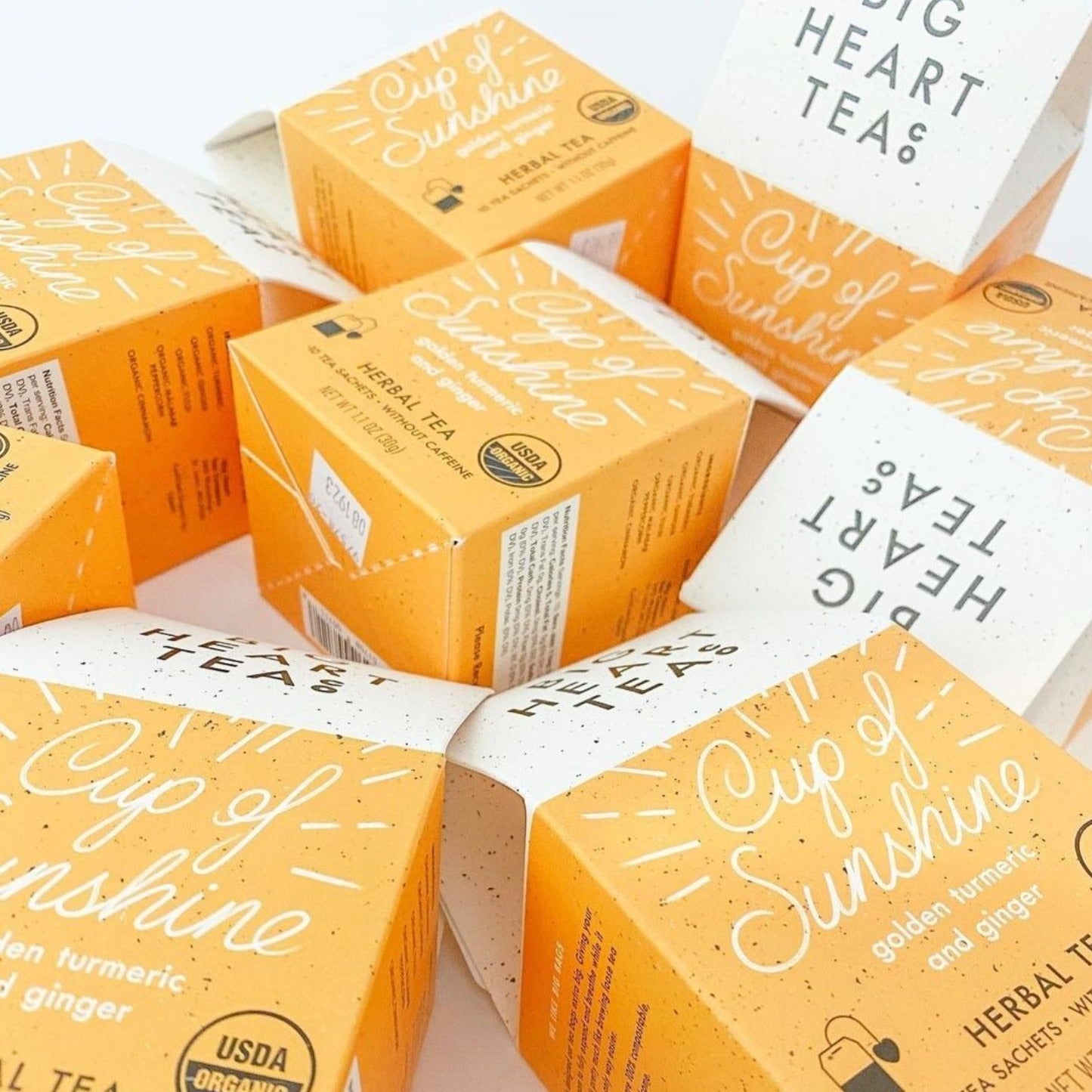 a bunch of yellow boxes of Big Heart Tea Co.'s Cup of Sunshine tea, an organic blend featuring turmeric, ginger, tulsi, Malabar peppercorn, and cinnamon. Known for its anti-inflammatory benefits, immune-boosting properties, and digestive aid.