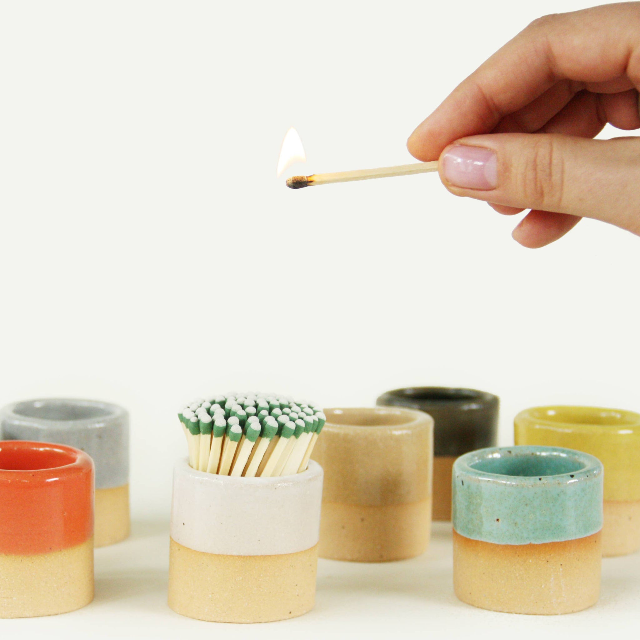 Hand lighting a match from the white ceramic match striker, showcasing its practical and stylish design.