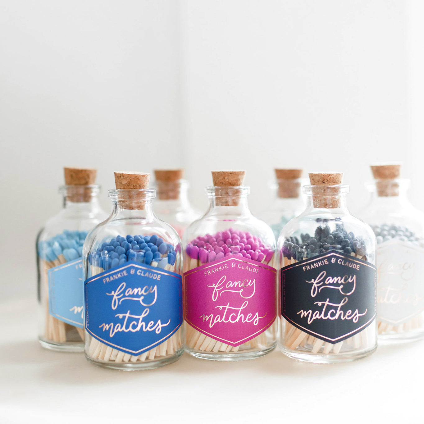 Assorted Frankie & Claude Fancy Matches in apothecary jars, showcasing different colors like blue, pink, and black for stylish candle lighting.