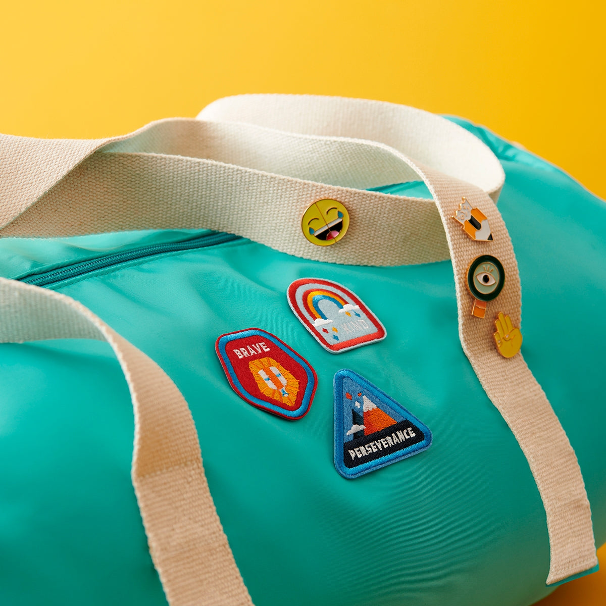 Set of 4 Character Badge Patches designed for children, featuring the words 'Creative, Funny, Team Player, Optimist' with vibrant colors, adhesive and iron-on backing, displayed on a aqua blue duffle bag.