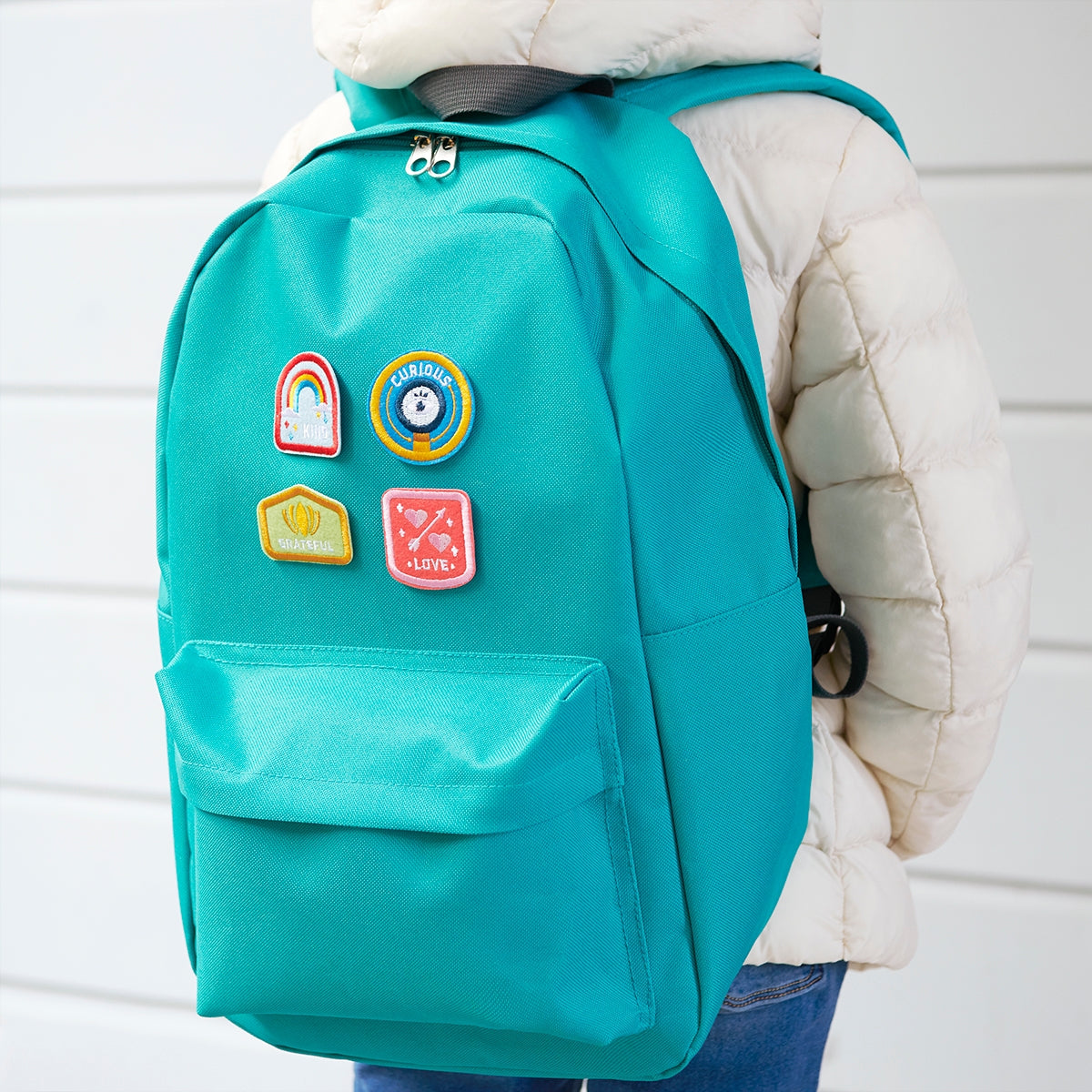 Set of 4 Character Badge Patches designed for children, featuring the words 'Creative, Funny, Team Player, Optimist' with vibrant colors, adhesive and iron-on backing, displayed on a aqua blue backpack.