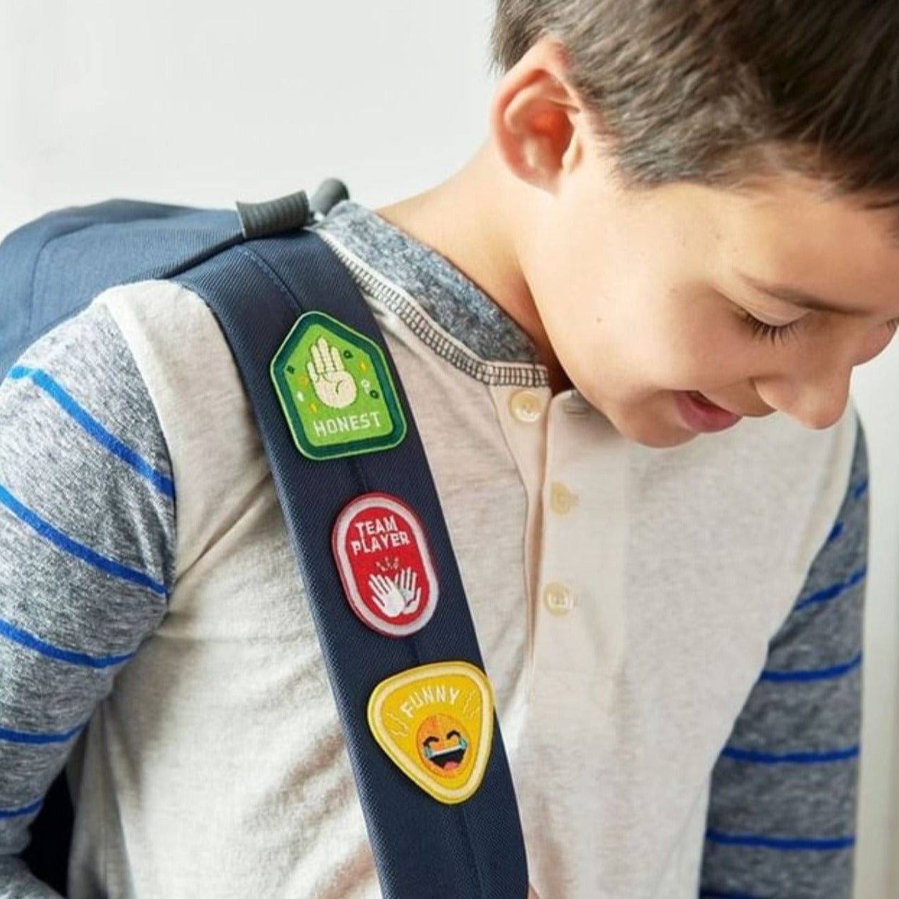 Set of 4 Character Badge Patches featuring the traits Curious, Honest, Brave, and Perseverance, shown on a backpack strap worn by a young boy, designed for children and ideal for backpacks or clothing. Adhesive and iron-on backing for easy application.