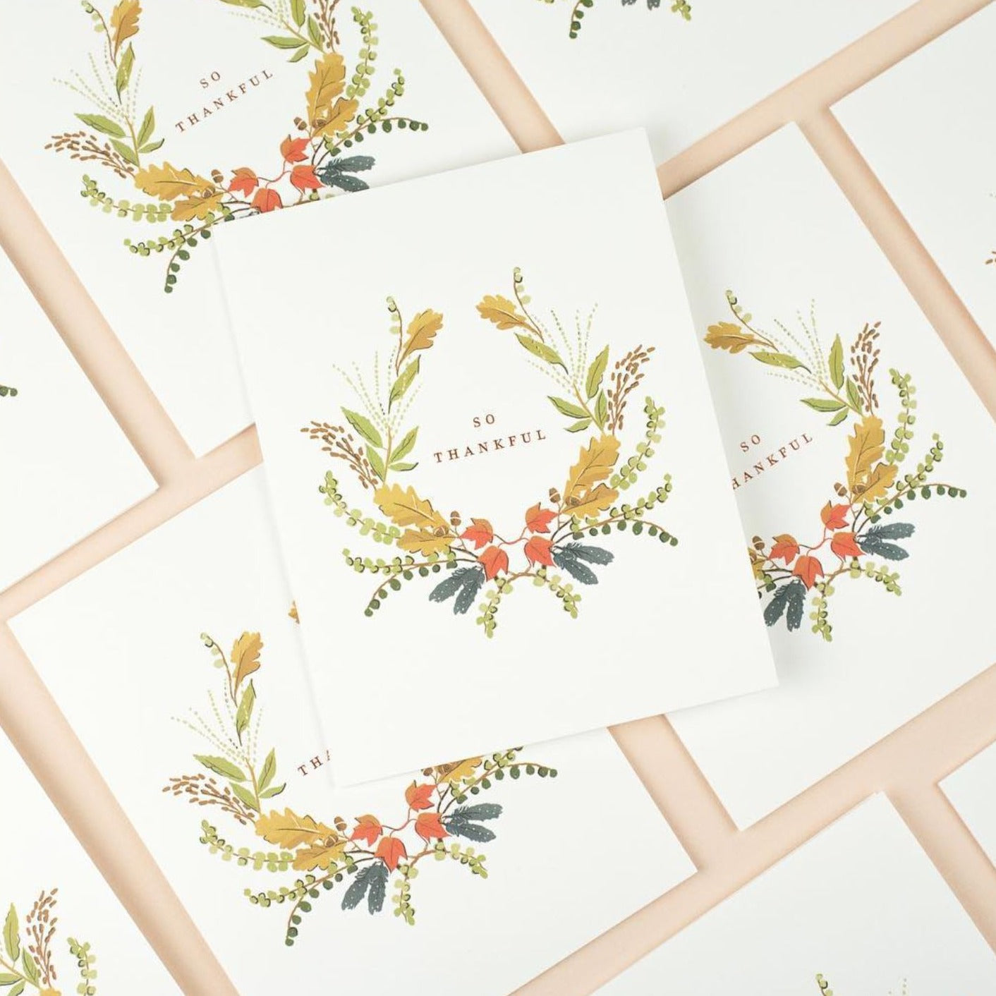 Illustrated Thanksgiving card with a wreath of fall-colored florals surrounding the gold foil words 'So Thankful' on warm white cardstock.